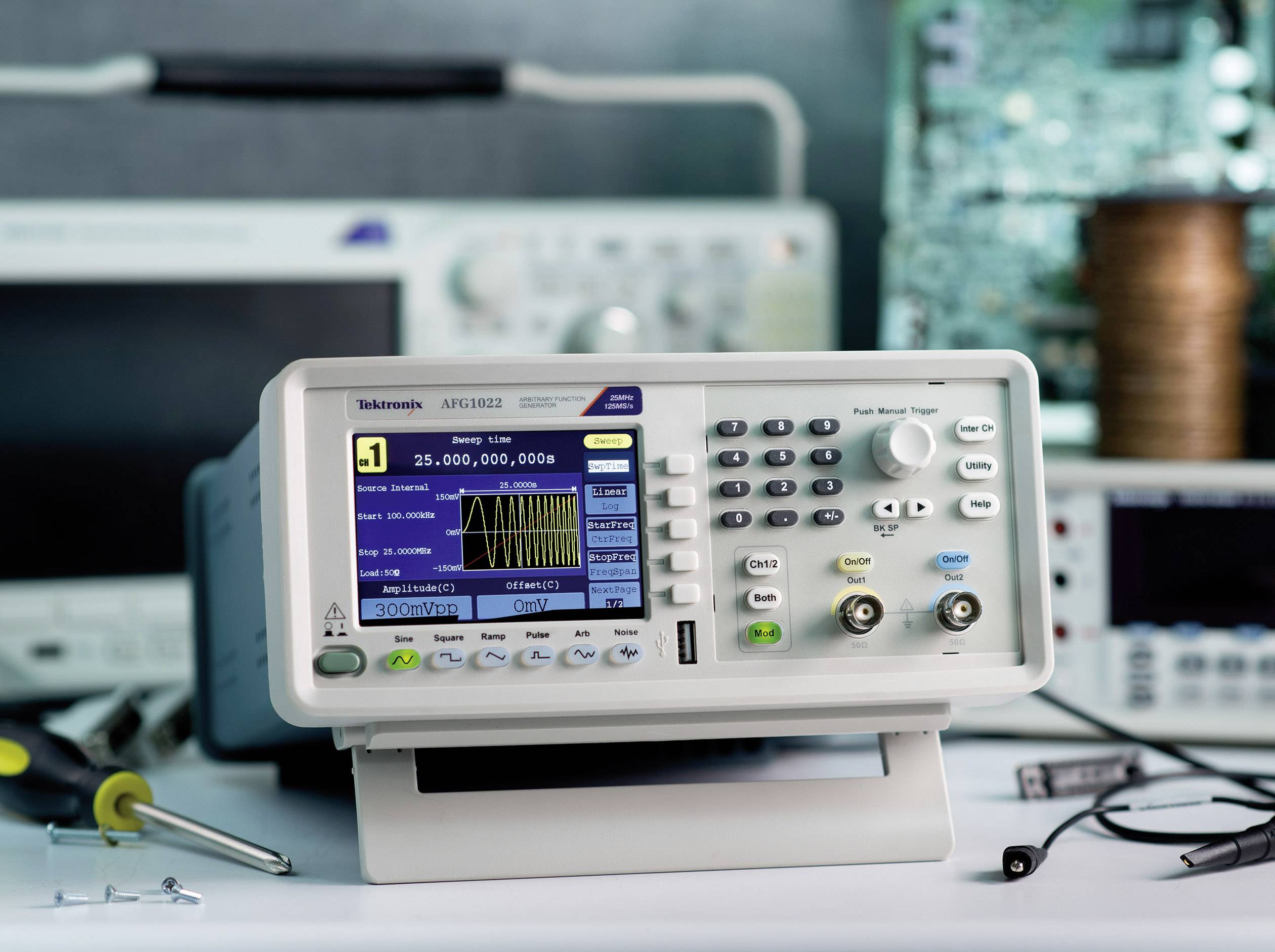 An oscilloscope on a table displays a graphical representation of voltage waves. Electronic devices and tools are visible in the background.