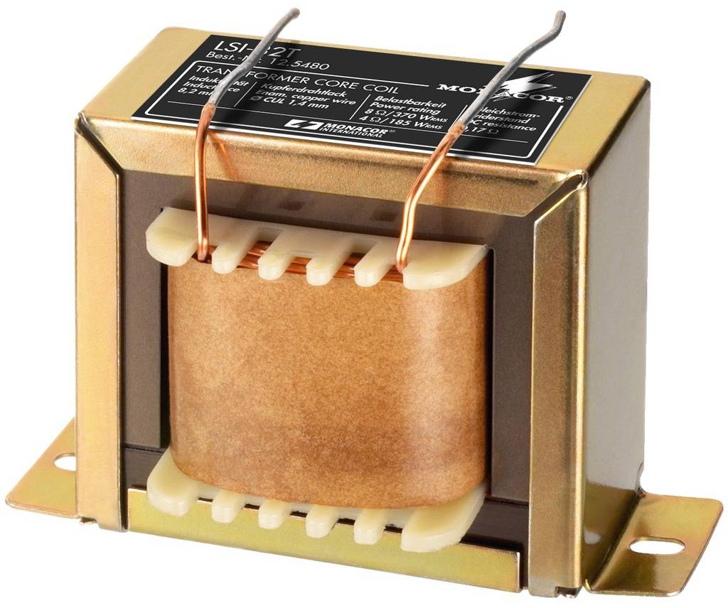A metal transformer with cable connections, standing on a table. It has a label with technical specifications on top.