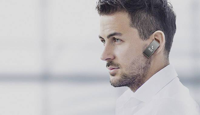 A man is wearing a wireless earphone headset and looking intently forward. The background is blurred, with the focus on the technology.