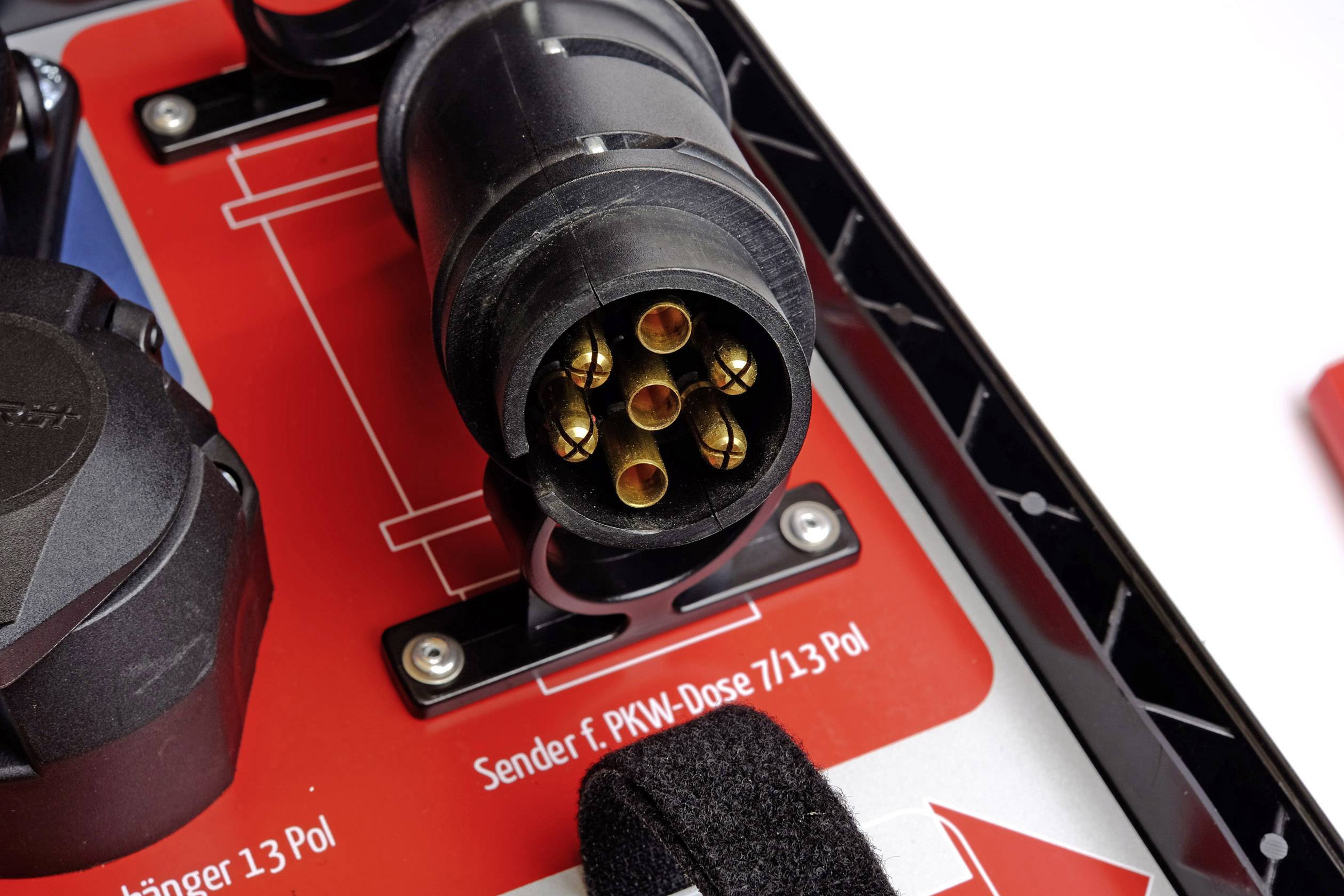 '13-pin trailer plug in close-up, connected to a vehicle socket adapter on a red background.'