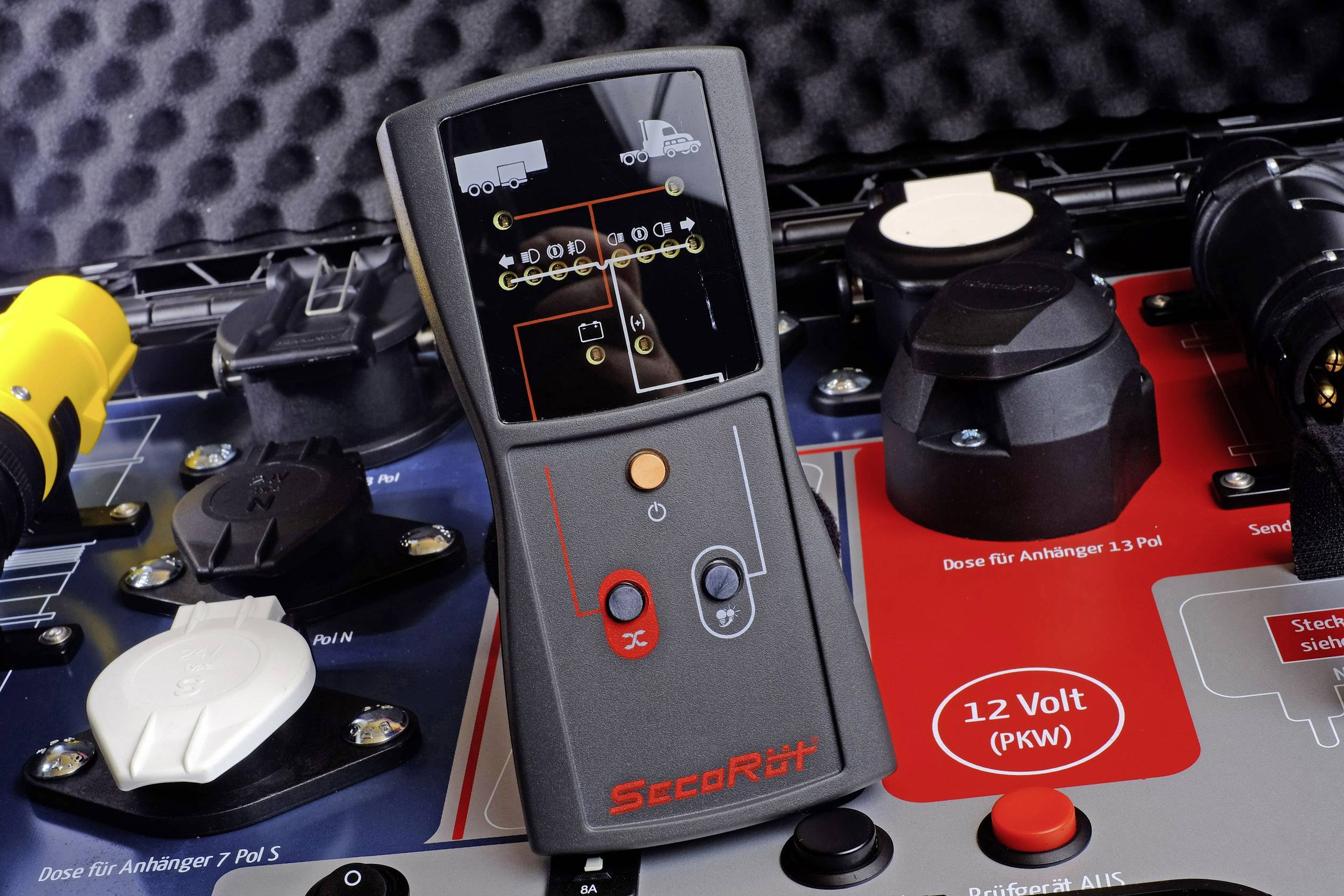 A black control unit with red buttons sits on a table with various sockets for trailers. Text reads 'SteerRite'.