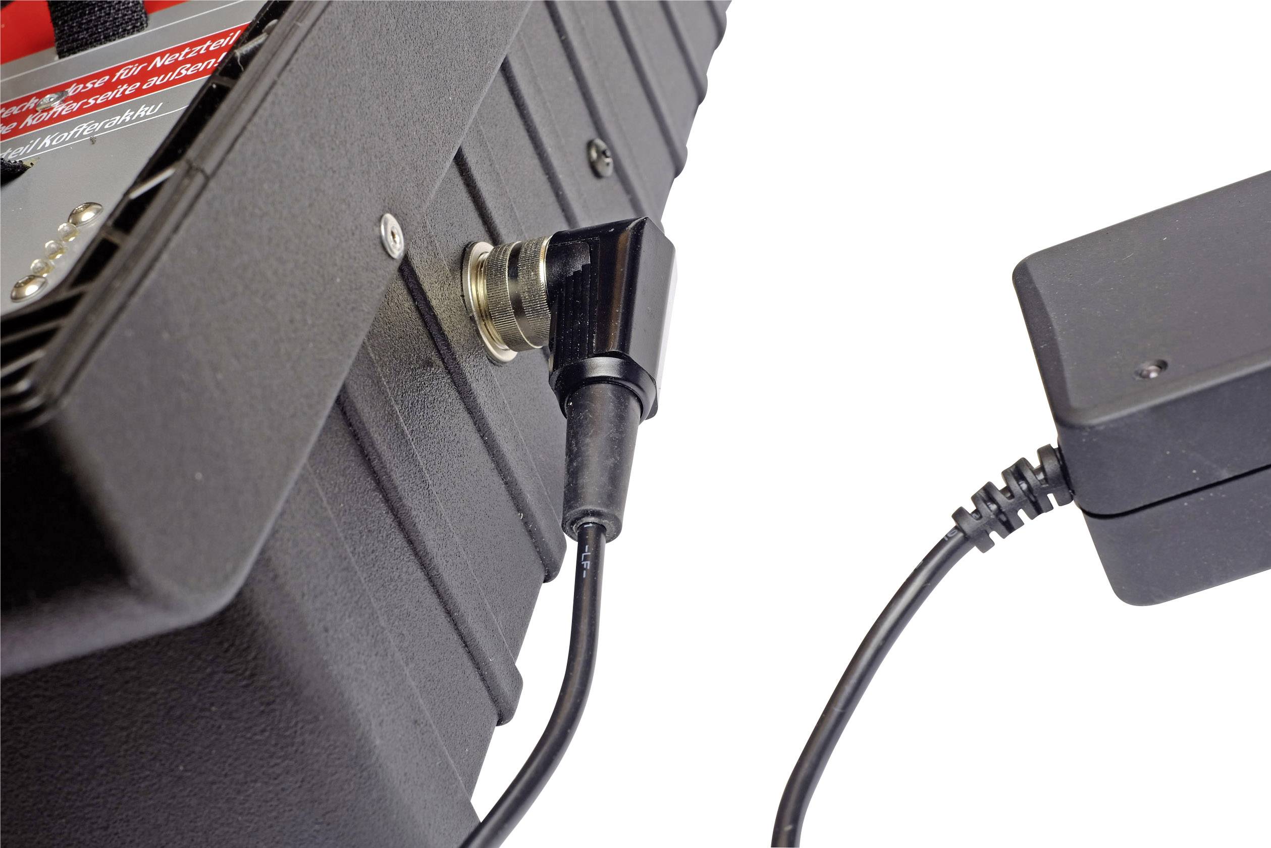 A black cable is plugged into a socket on an electronic device; next to it is a power adapter.