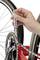 A hand is holding a tool and checking the chain tension of a bicycle mounted on a red frame.