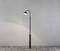 A simple lantern in a minimalist style stands on paved ground in front of a grey wall.