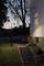 A white house at dusk with an illuminated window and lantern, in front of a garden staircase, surrounded by trees and lawn.