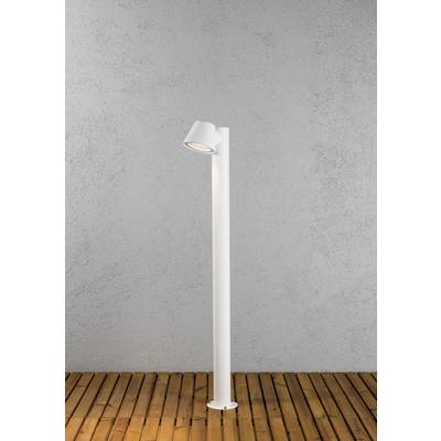 A simple, white standard lamp stands on a wooden floor in front of a grey wall. The lamp is casting light downwards.