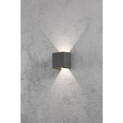 A grey wall light projects an X-shaped light pattern onto a roughly textured grey wall.