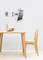 Tablet on a movable wall mount above a wooden table with a vase and cup, next to a wooden chair against a light wall.