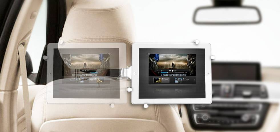 Tablets mounted on seat backs display films on screens. Rear seat view of a car, focusing on passenger entertainment.