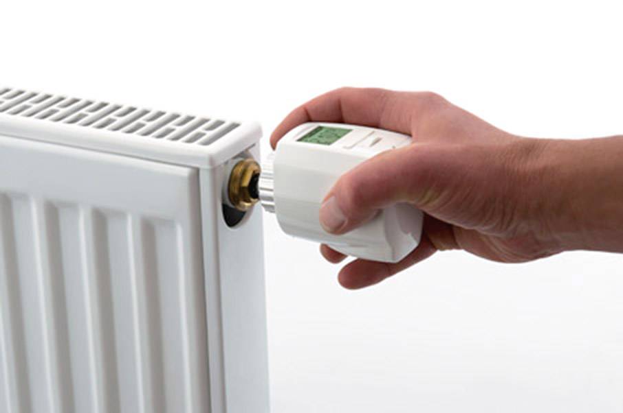A hand turns the thermostat of a white radiator.