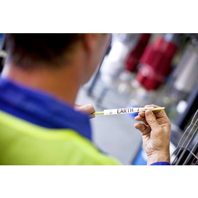 A man is holding a yellow pen with the inscription 'EARTH'. He is wearing a work jacket, with blurred tools in the background.