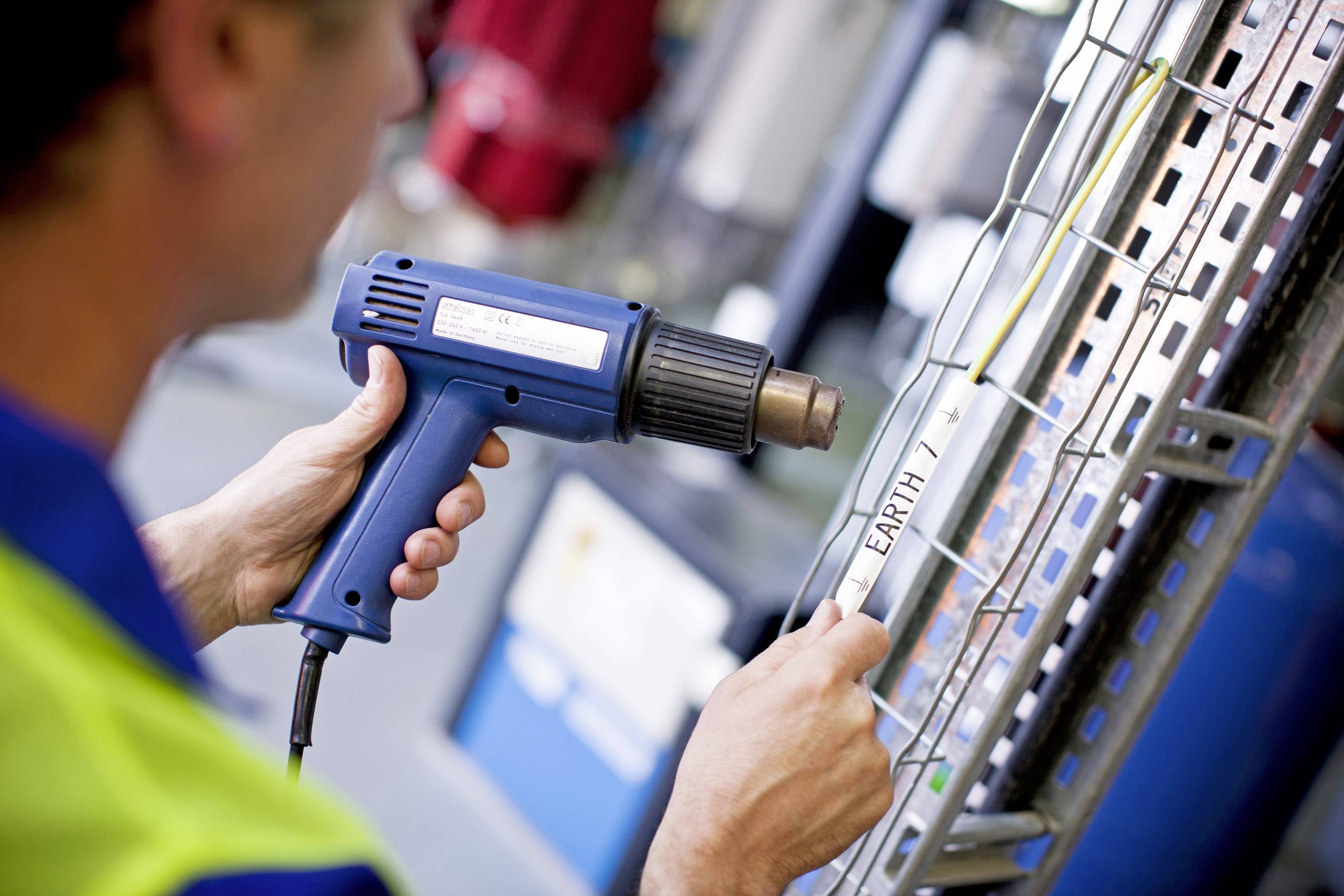 A person is using a hot glue gun to attach a label reading 'EARTH' to a metal shelf.