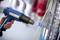 A person is using a blue heat gun to seal heat-shrink tubing on cables. Blurred objects are visible in the background.