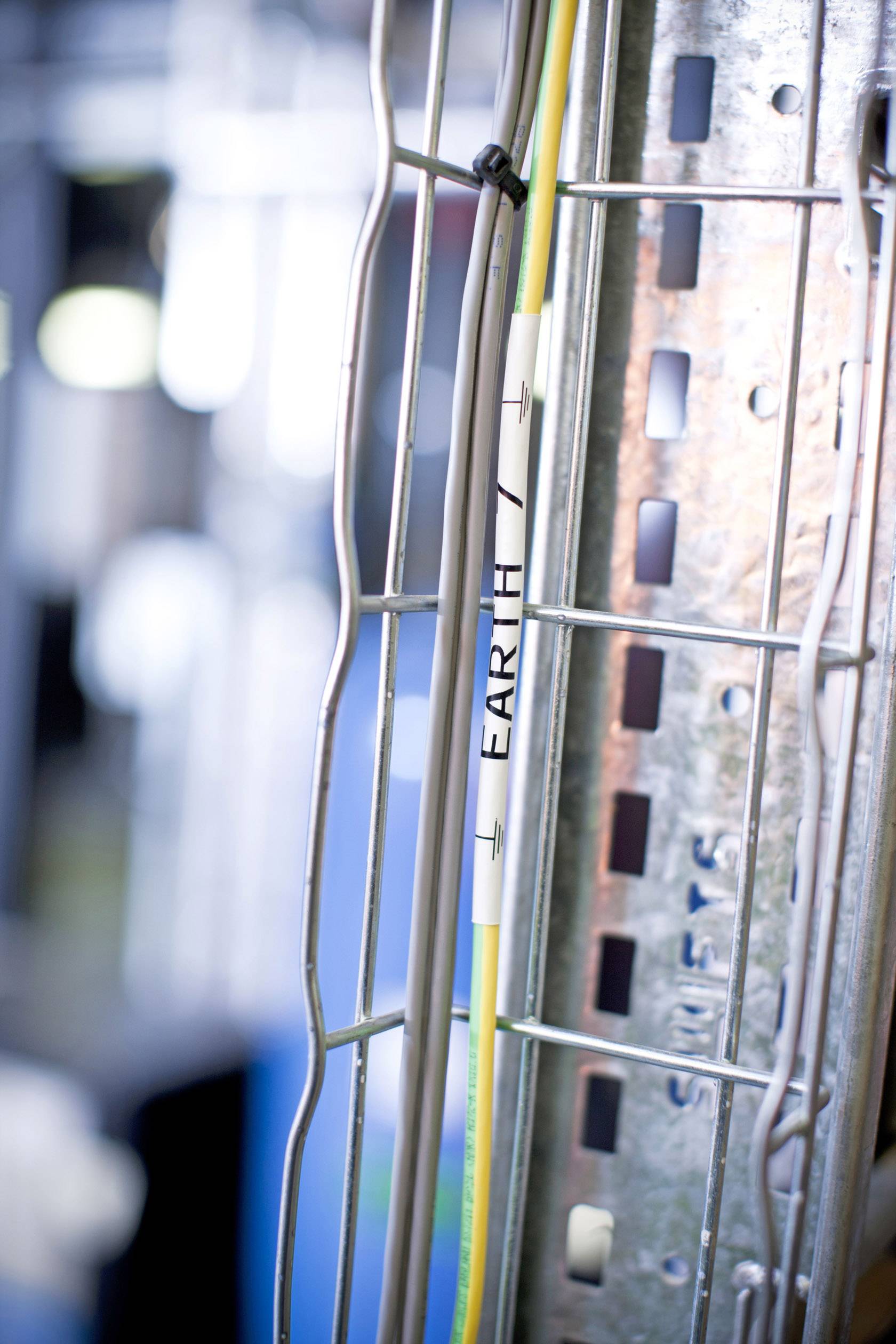A yellow cable marked 'EARTH' is attached to a metal lattice structure. Industrial elements are visible in the blurred background.