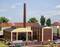 Model of an industrial site with large buildings and a chimney. Several cars are parked on the street.