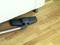 A vacuum cleaner is cleaning the wooden floor beneath a white sofa to remove dust and dirt.