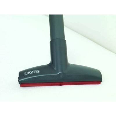 A vacuum cleaner attachment is sucking a white surface. The attachment is dark with a red rubber strip and the 'Thomas' brand.