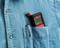 A multimeter is tucked into the breast pocket of a blue shirt. It displays '8888' on the screen. A pen is beside it.