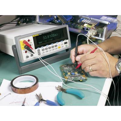 A technician is measuring the electrical voltage on a circuit board using a multimetre. Tools and circuit details are visible in the background.