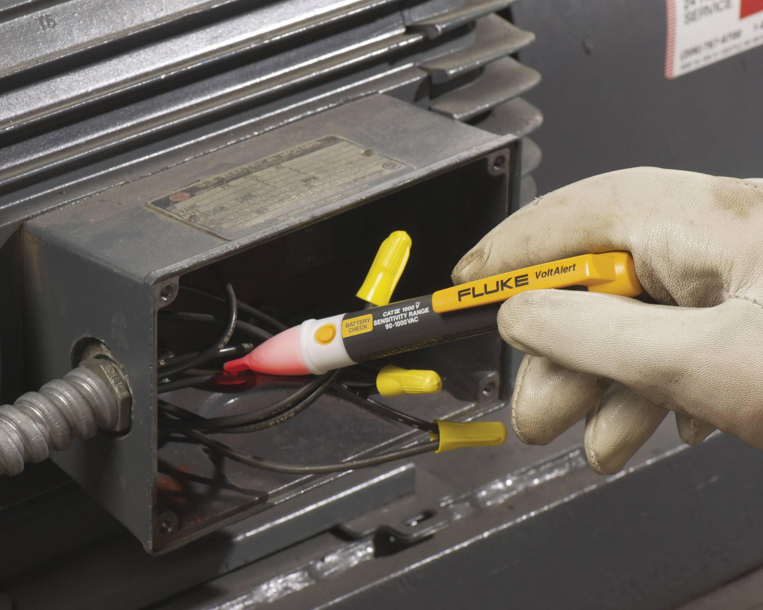 A hand is holding a voltage tester being used on an open electrical panel to test the voltage of cables.
