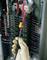 An electrician's glove holds a voltage tester near a fuse box full of cables to check the voltage.