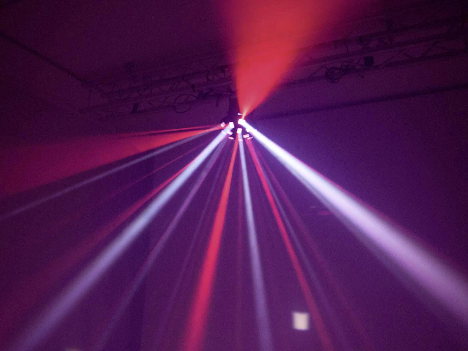 Red and white light rays spread out radially in a dark room, creating a vibrant light spectacle.