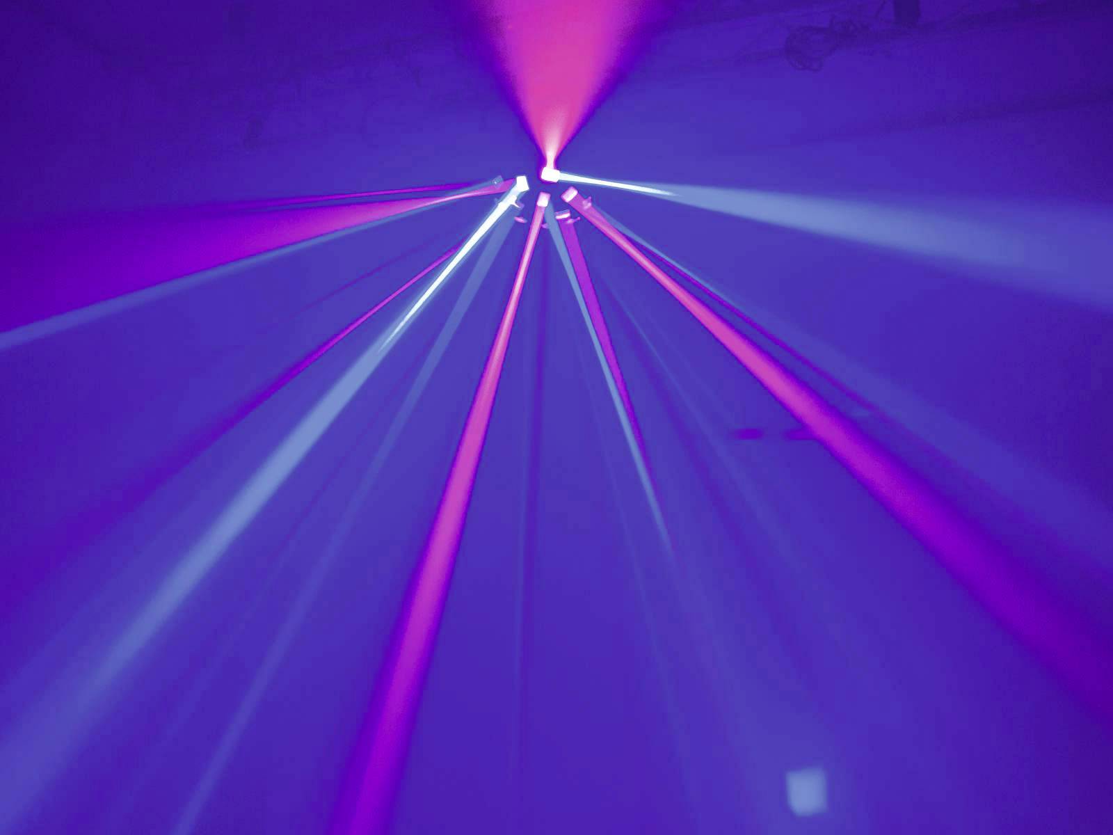 Colourful laser beams in blue and purple tones slice through the darkness in a room, creating a vibrant light display.