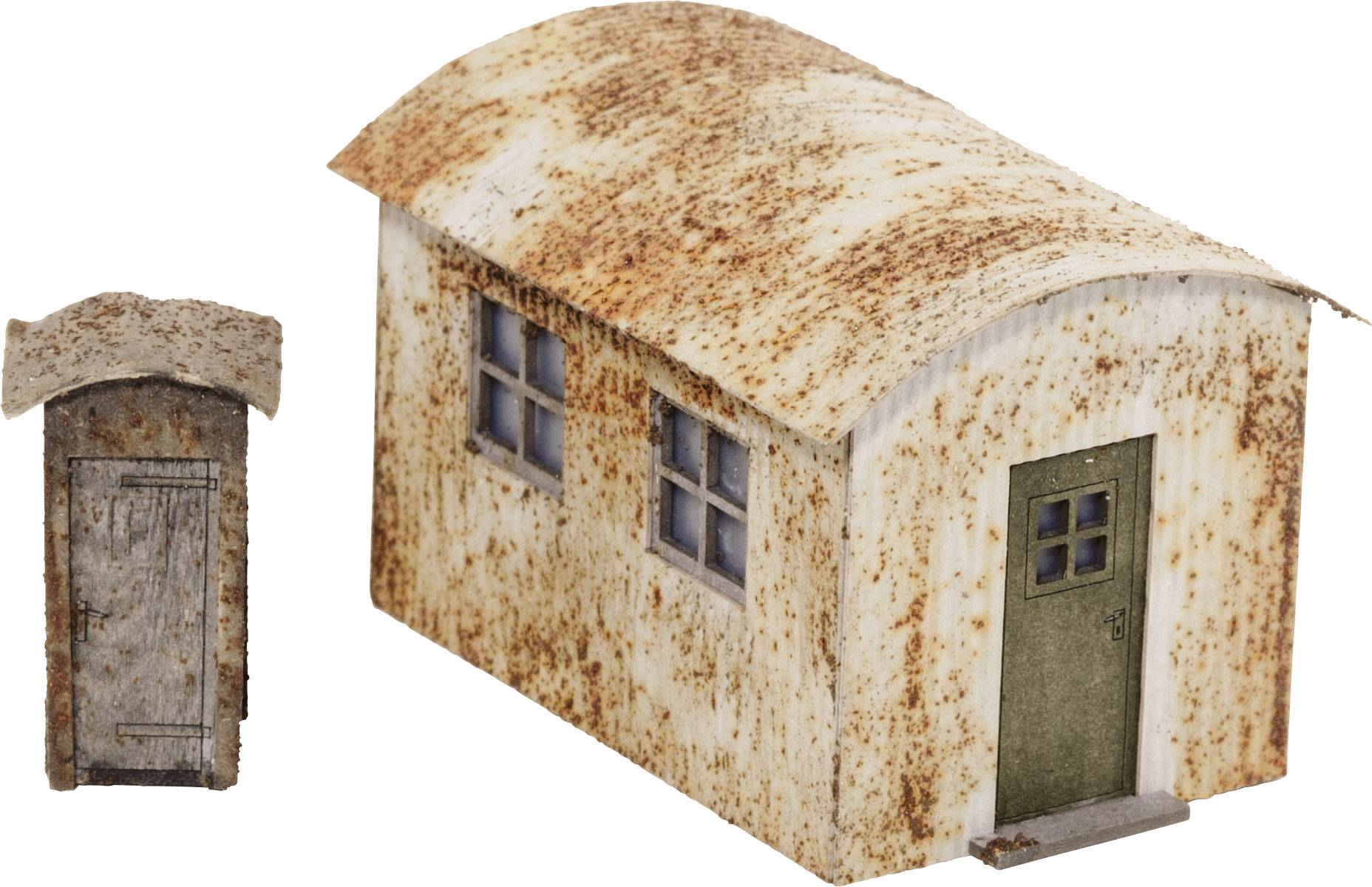 A rusty miniature building with two windows and a green door, with a small matching lavatory beside it.