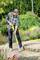 A man is cleaning a paved garden path with a yellow pressure washer. Flower beds are visible in the background.