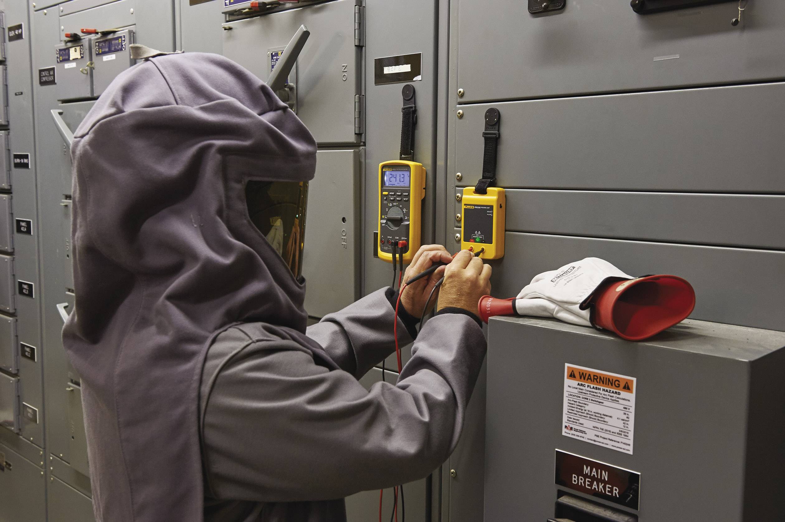 A person wearing protective equipment is working with a multimeter on an electrical cabinet to carry out electrical measurements.
