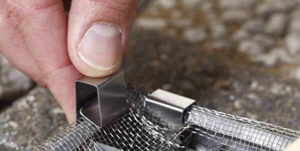 A hand is securing a wire mesh with a small metal clip onto a surface.