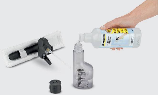 A hand is pouring cleaning solution into an empty spray bottle. Next to it lies a cleaning device with a white cloth and a cap.