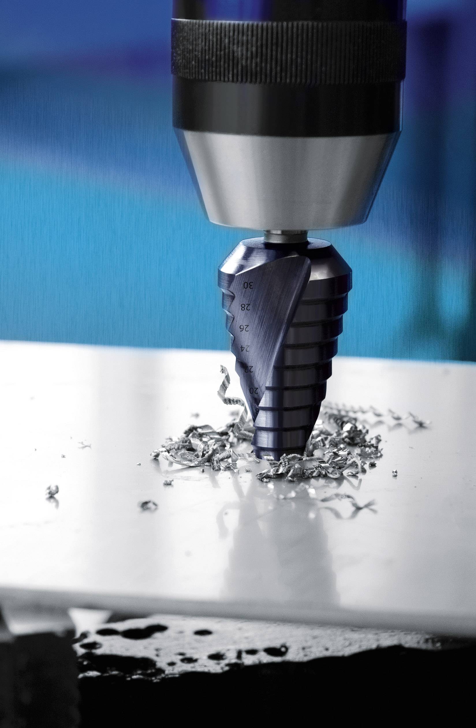 A stepped drill bit is piercing a metal sheet, with metal shavings around the hole. The scene depicts a precise drilling process.