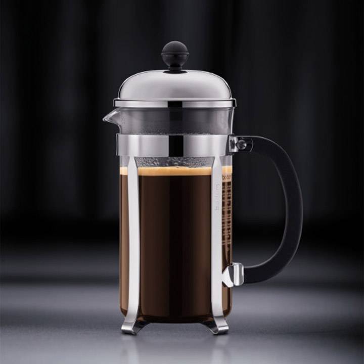 A French press coffee pot filled with freshly brewed coffee on a dark background.