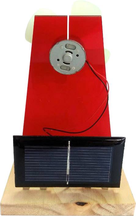 A red solar model with a fan on top, powered by a solar panel on a wooden platform.