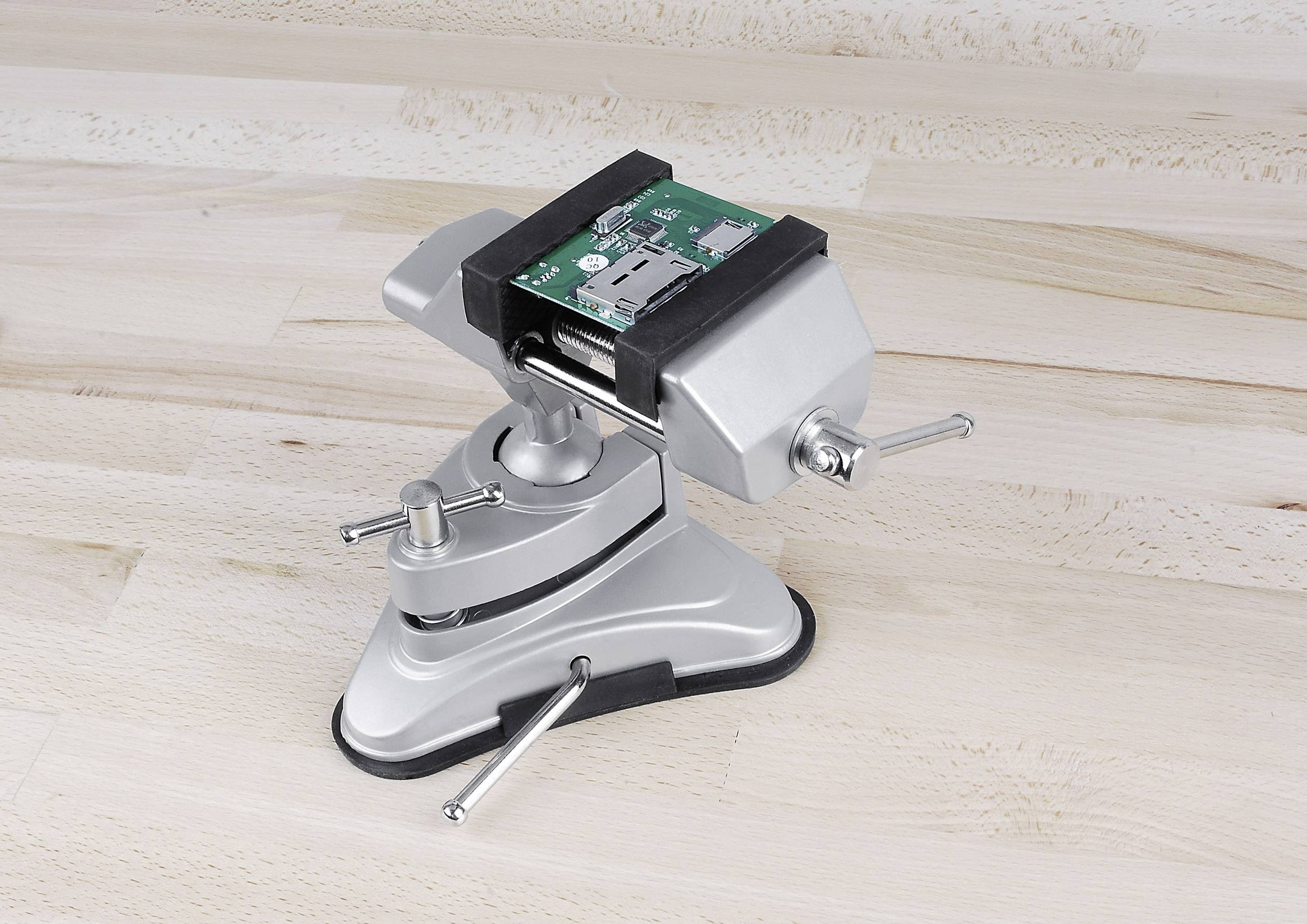 A vice is holding a green circuit board firmly. The vice is situated on a wooden surface.