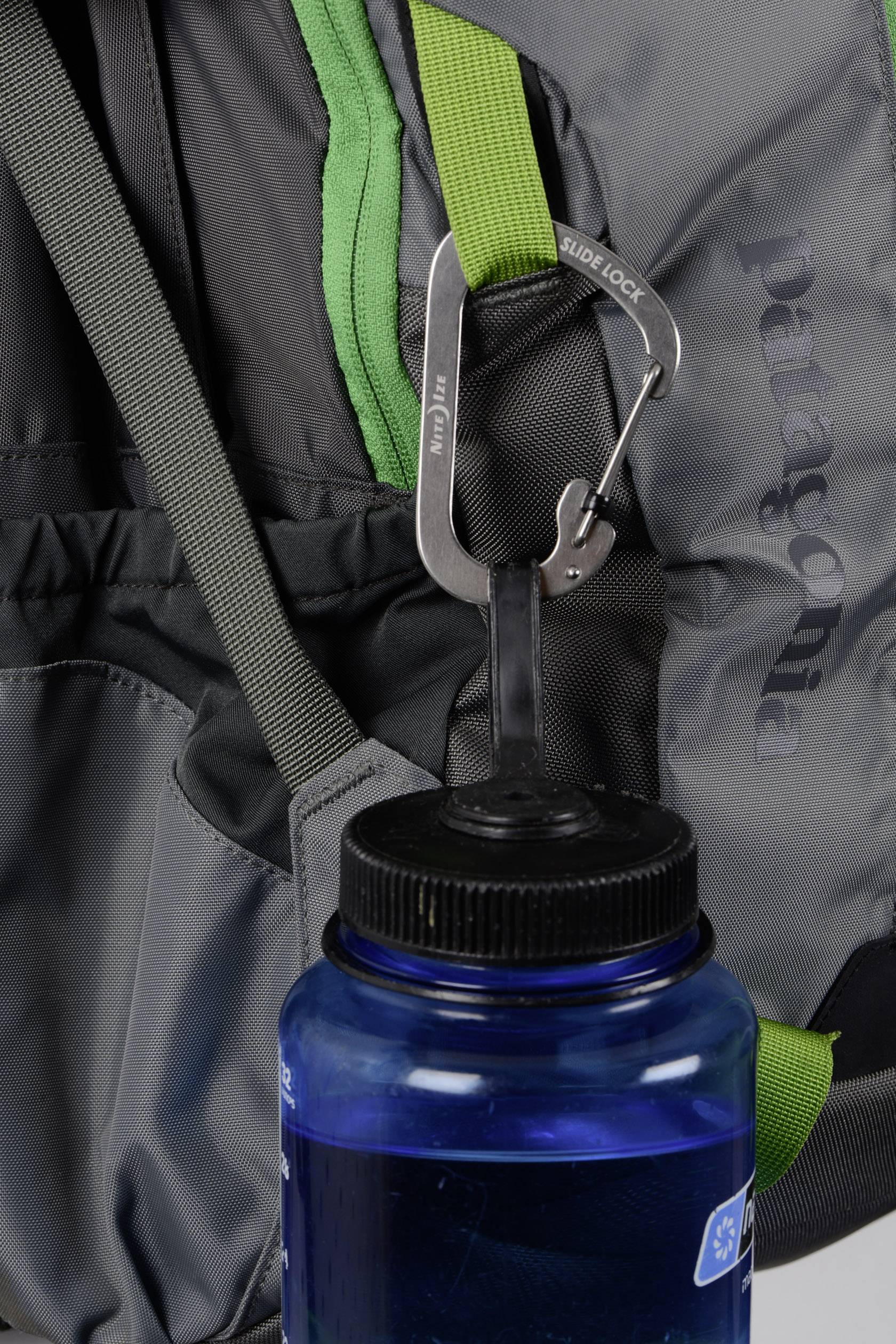 A grey rucksack with a green handle, to which a silver carabiner is attached, holding a blue water bottle.