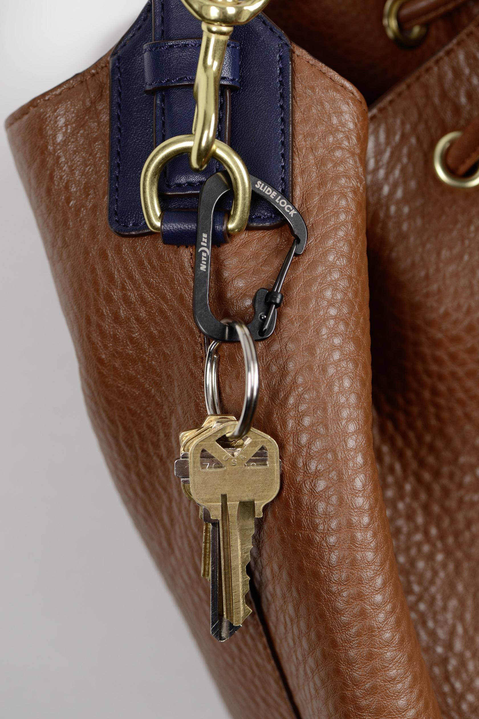 A brown leather pouch with a gold-coloured carabiner clip, to which a bunch of keys is attached.