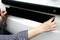 A person is attaching a black shield to a white vehicle, possibly a number plate or parking protection.