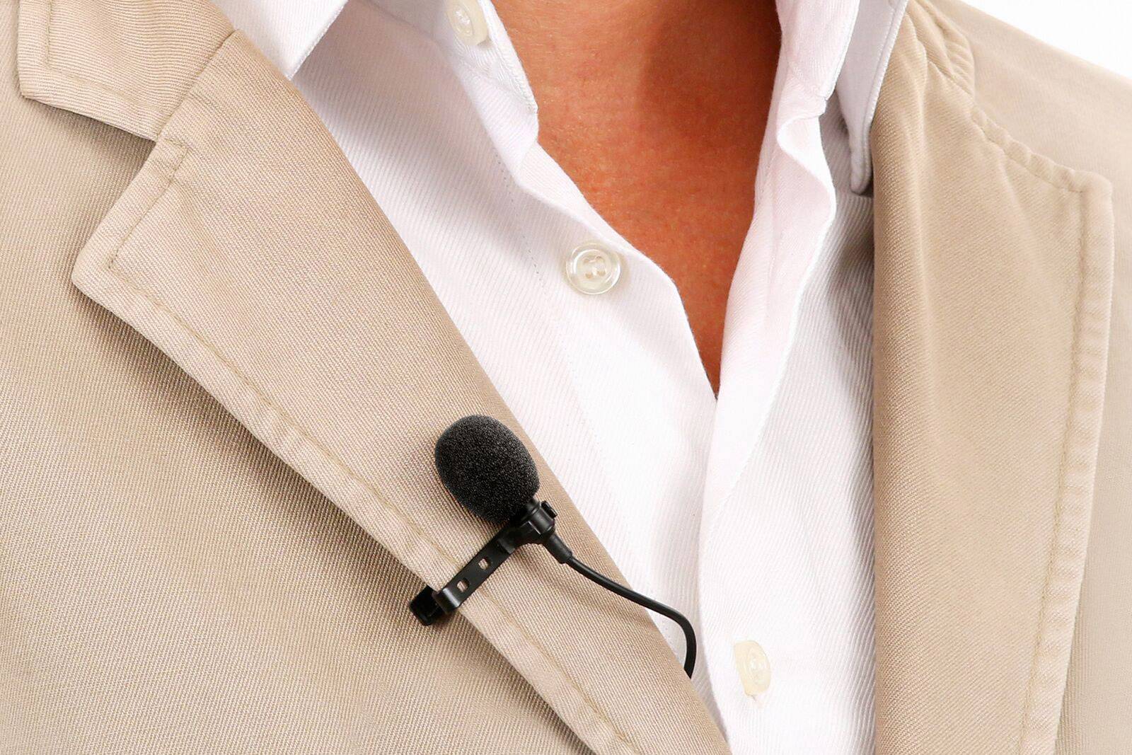 A person wearing a beige blazer with a white shirt has a lapel microphone attached to their jacket.