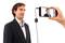 A man in a suit is speaking into a microphone, while someone records a video of him on a mobile phone.