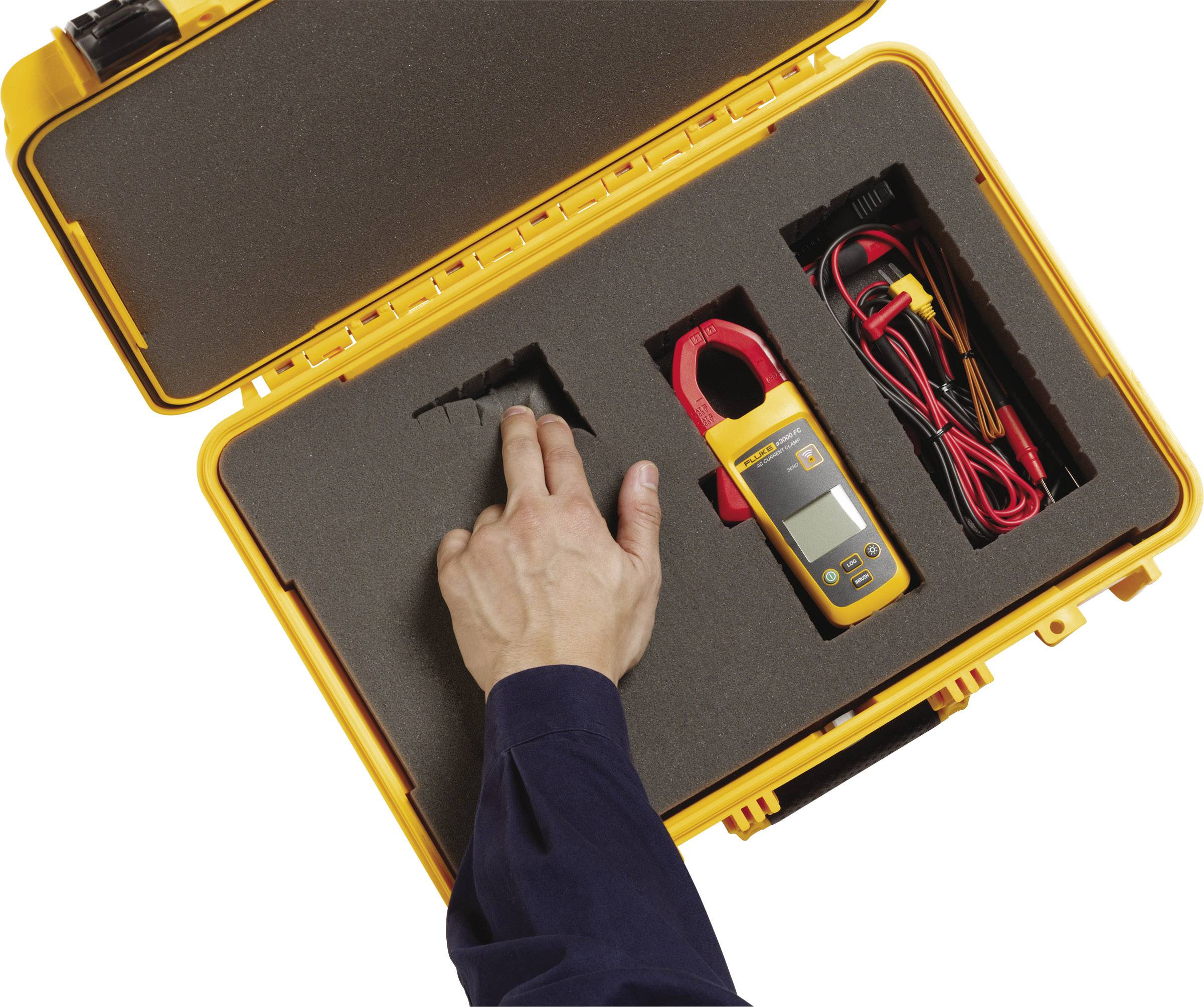 'A case with foam lining contains a yellow measuring device and cables. A hand points to an empty compartment.'