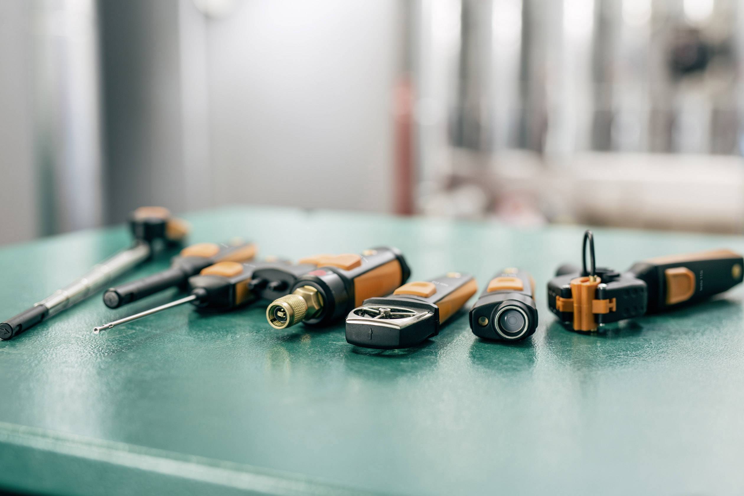 On a green table, various tools are laid out, including screwdrivers and pliers. The background is out of focus.