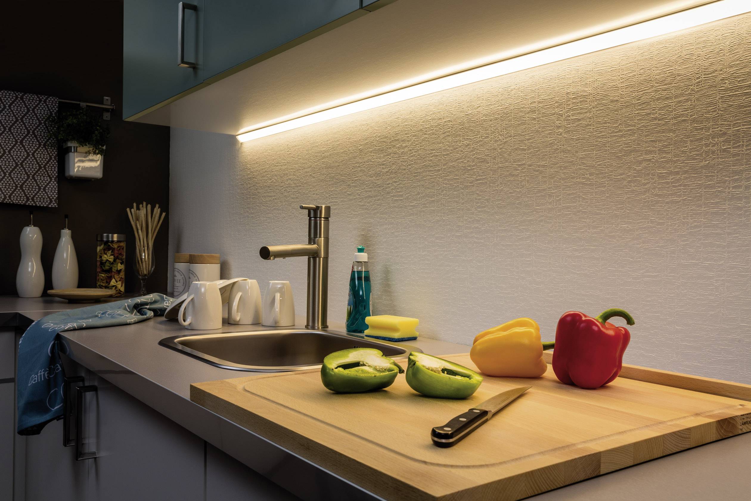 Fully equipped kitchen with illuminated shelf, chopping board with colourful peppers and knife on the worktop.