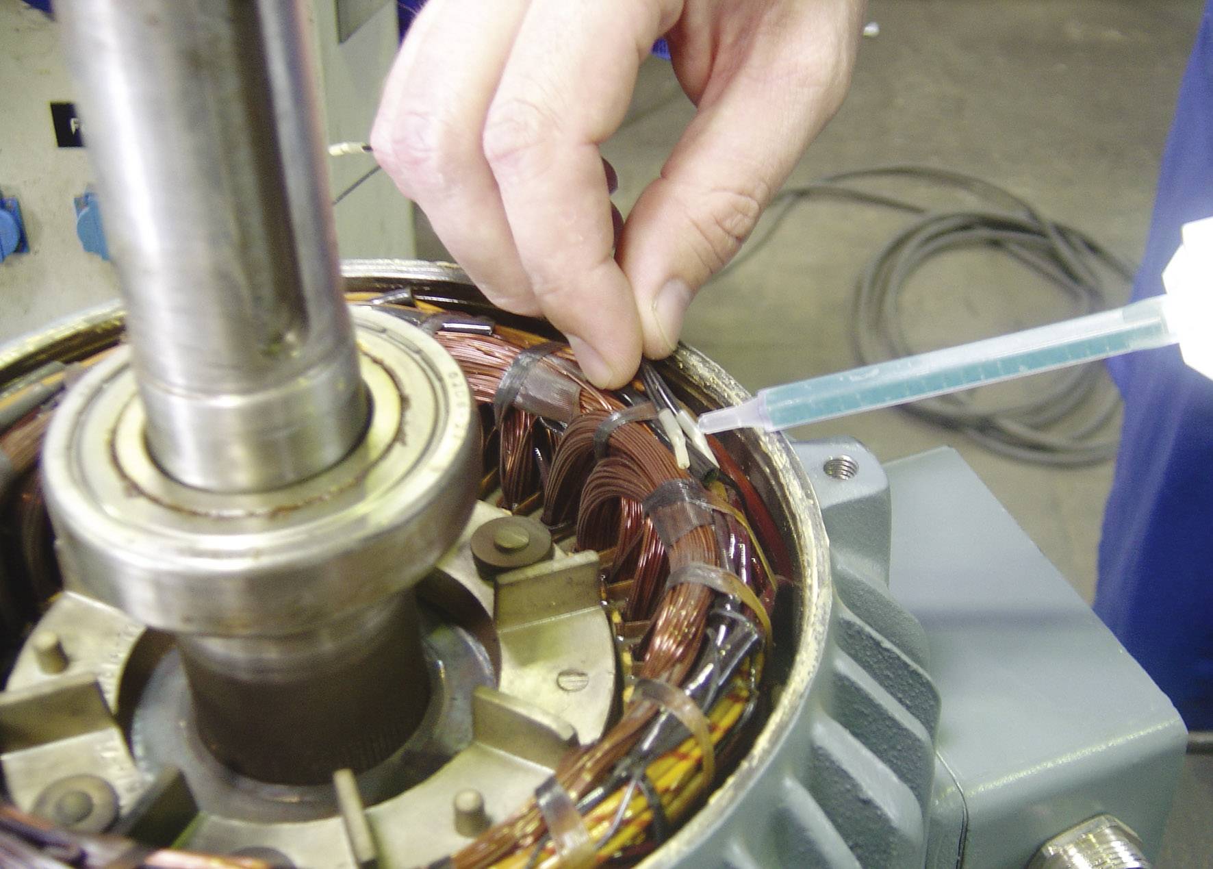 A person is repairing an electric motor, injecting liquid into the copper windings. The surroundings suggest a workshop.