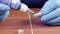 'A person wearing blue gloves is applying adhesive to a metal thread to secure it.'