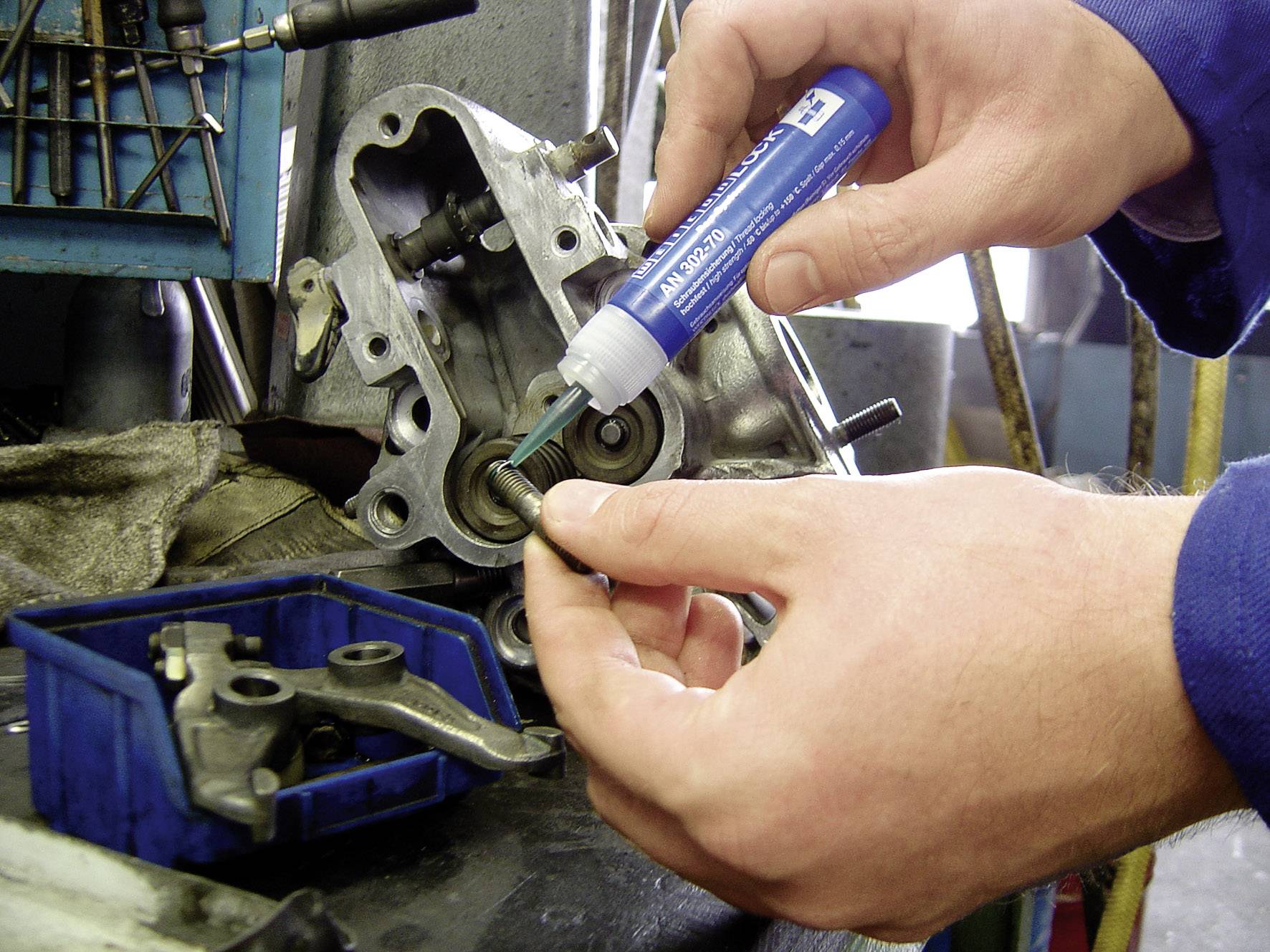 A person is applying a lubricant with a bottle of blue liquid to a metal part that is attached to a machine component.