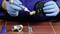 A person wearing blue gloves is applying sealant to a brass pipe thread. A T-piece and an adapter are lying in front of it.