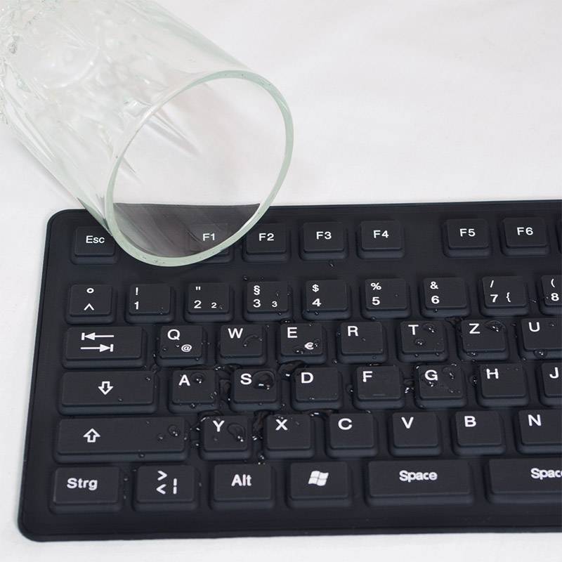 An overturned glass vase with water on a keyboard. Water droplets cover the keys, indicating potential damage.