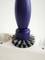 A blue cleaning brush with grey bristles sits on a white plastic housing. No further information in the image.